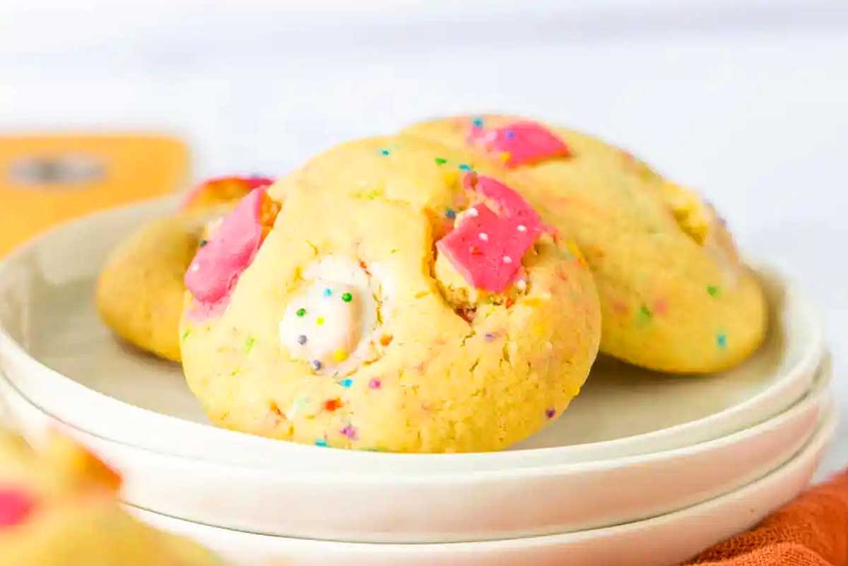 Plate of colorful sprinkle cookies, inspired by recipes that use circus animal cookies, with one cookie prominently showing a bite taken out, placed on a white ceramic plate against a bright background.