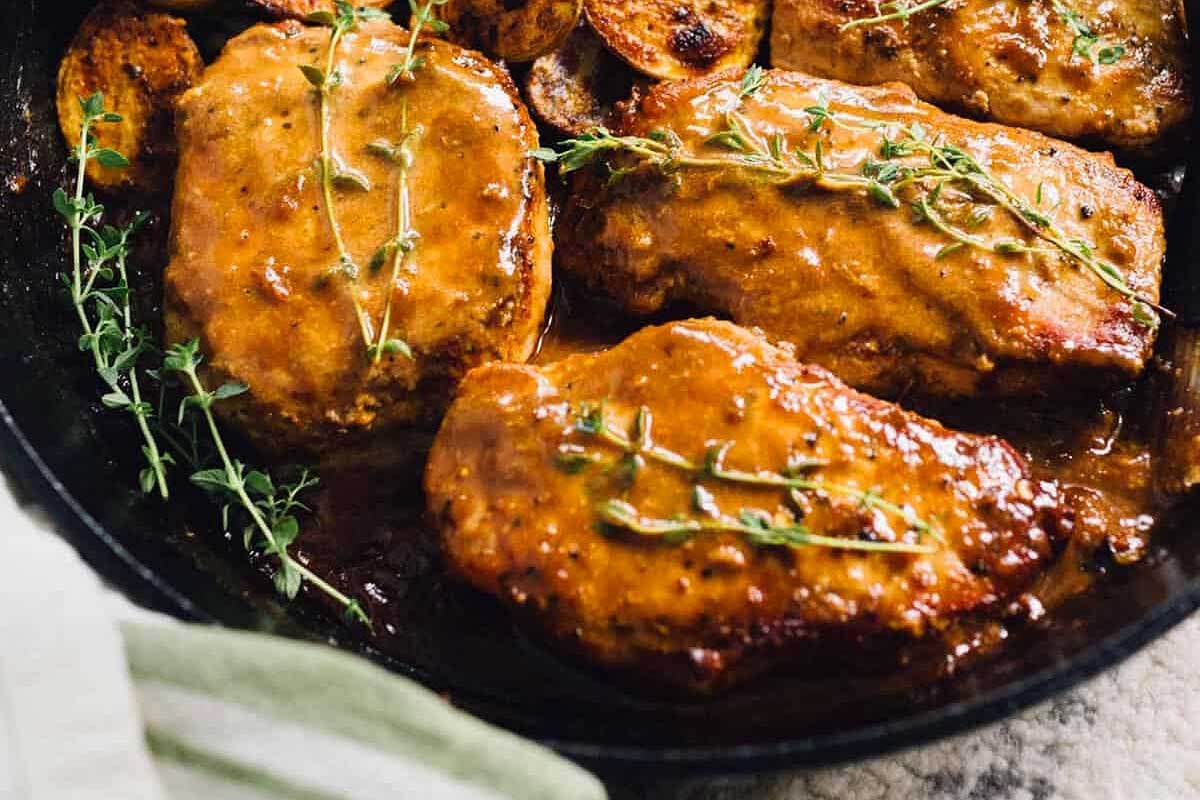 Pork chop recipes featuring pork chops with a glaze and fresh thyme in a skillet.