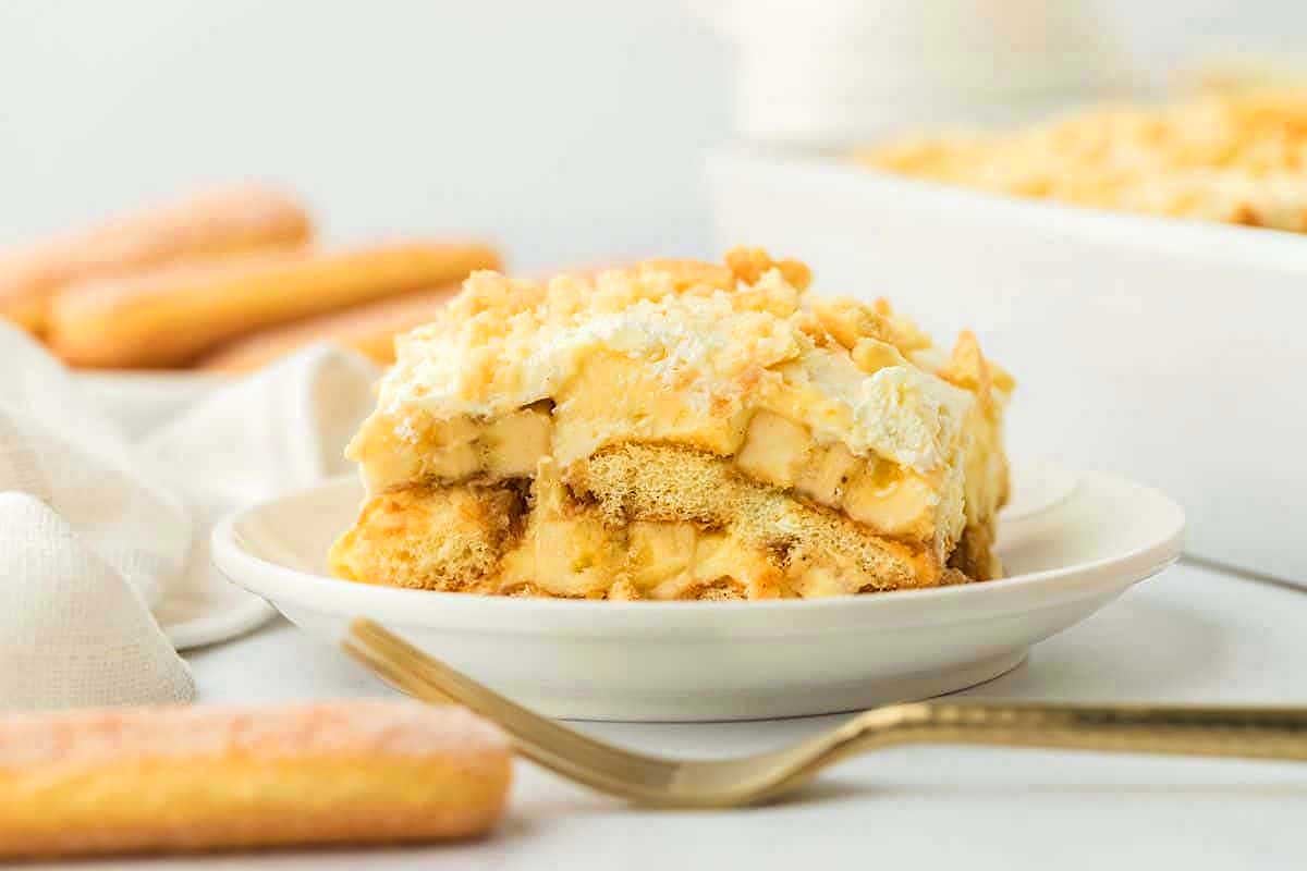 A slice of tiramisu with pudding mix on a plate with ladyfinger cookies and a dessert fork.