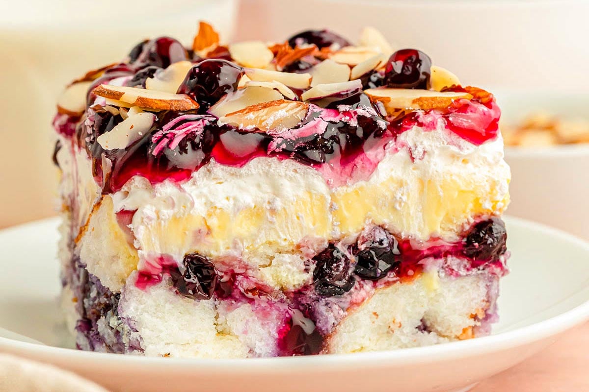 A slice of berry-topped cream cake with almonds on a white plate, perfect for church potluck desserts.