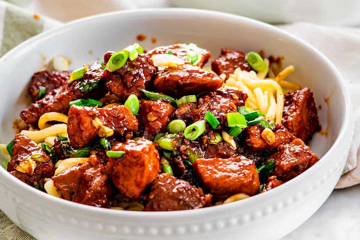 A bowl of general tso's chicken topped with green onions, served over noodles in 30 minutes or less.