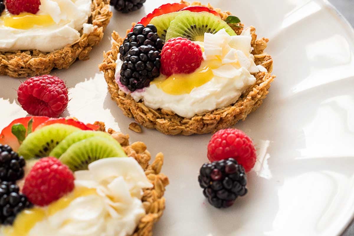 Granola cups filled with lemon curd and topped with various fresh fruits like blackberries, raspberries, kiwi, and strawberries on a white plate.