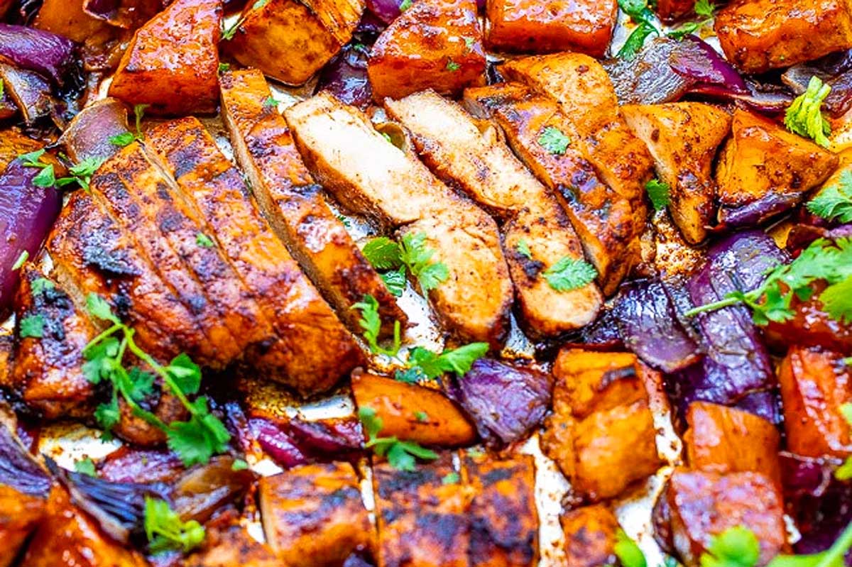 Grilled chicken breasts with slices of roasted sweet potatoes and red onions on a sheet pan, garnished with fresh parsley.