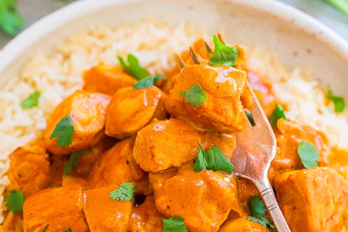 A bowl of creamy chicken tikka masala, ready in 30 minutes or less, garnished with fresh cilantro, served with steamed rice and a wooden spoon.