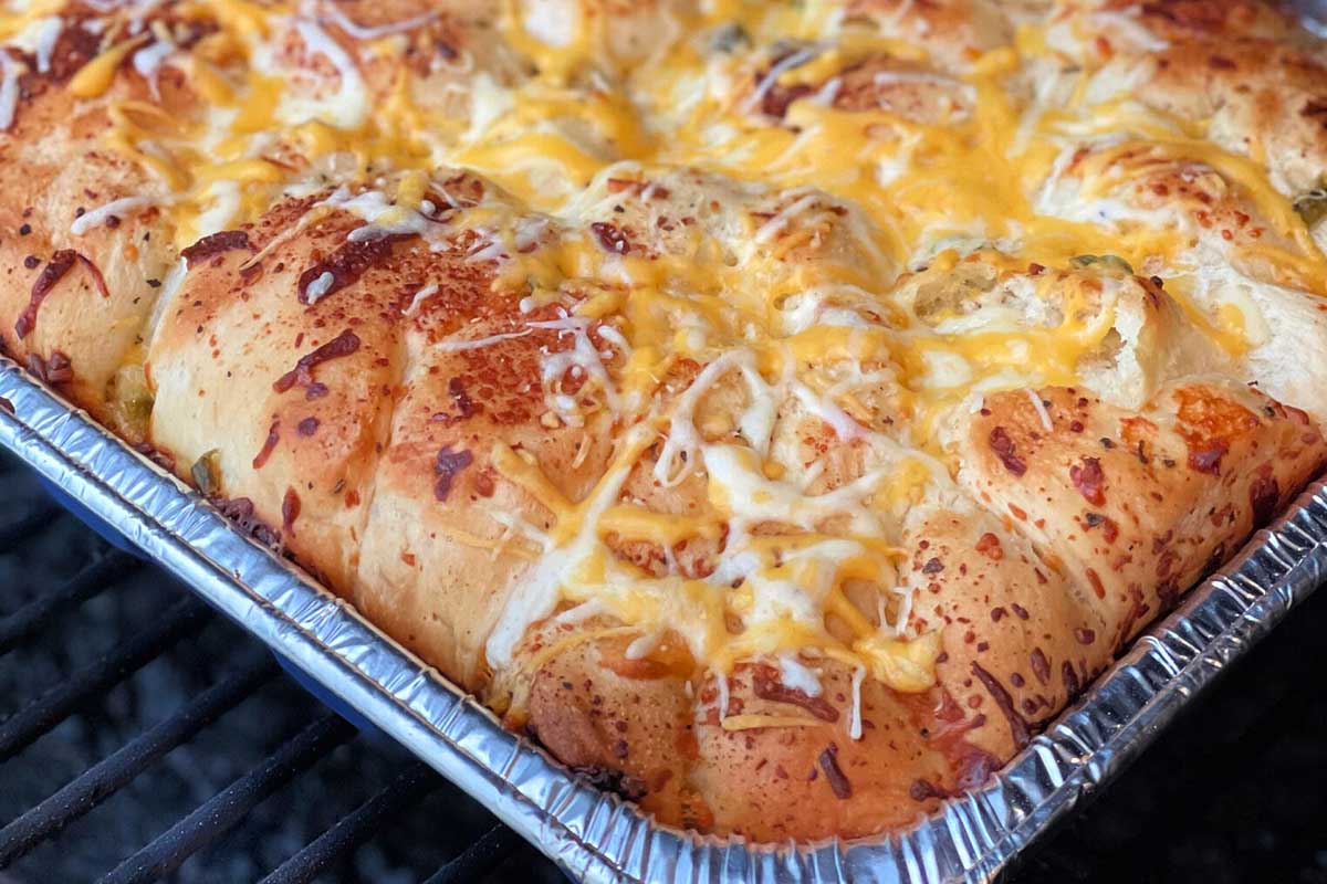 A tray of freshly baked pull-apart bread from smoker recipes, topped with melted cheddar and mozzarella cheese, showing a golden-brown crust.