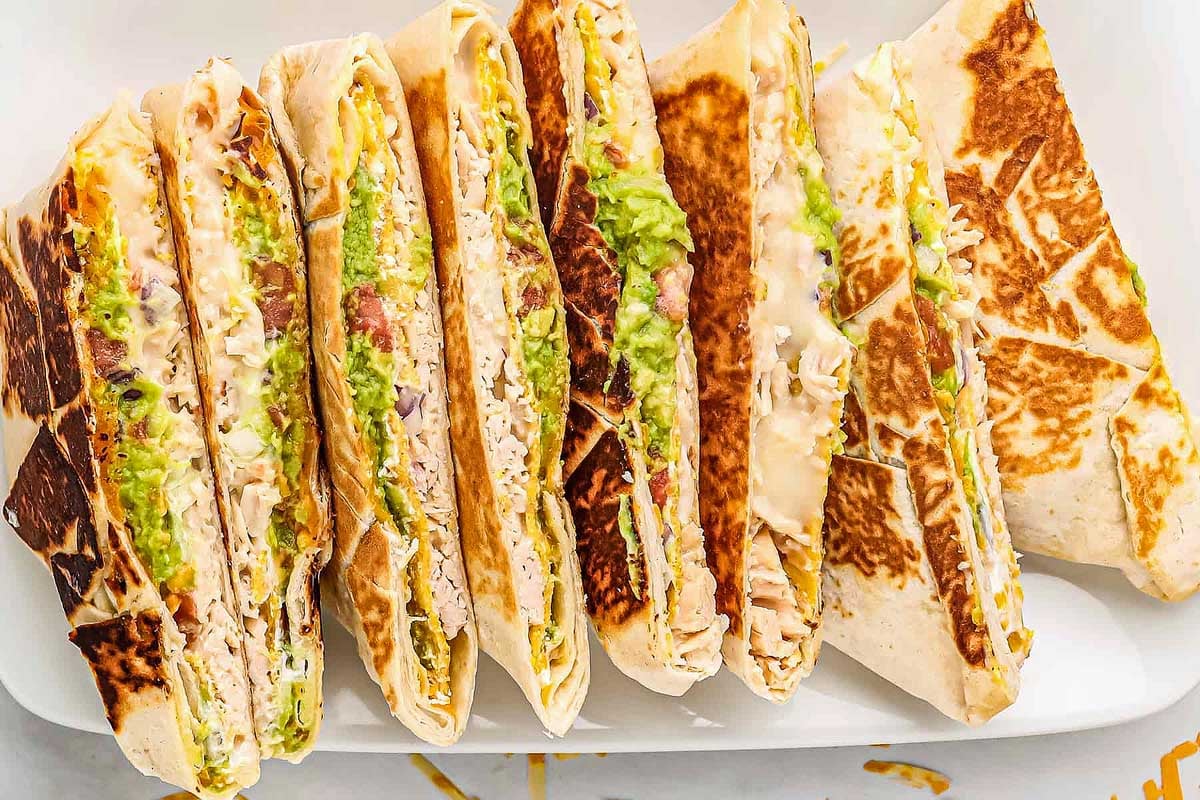 An assortment of Taco Bell copycat grilled wraps, each filled with ingredients like chicken, lettuce, and sauces, lined up on a white plate.