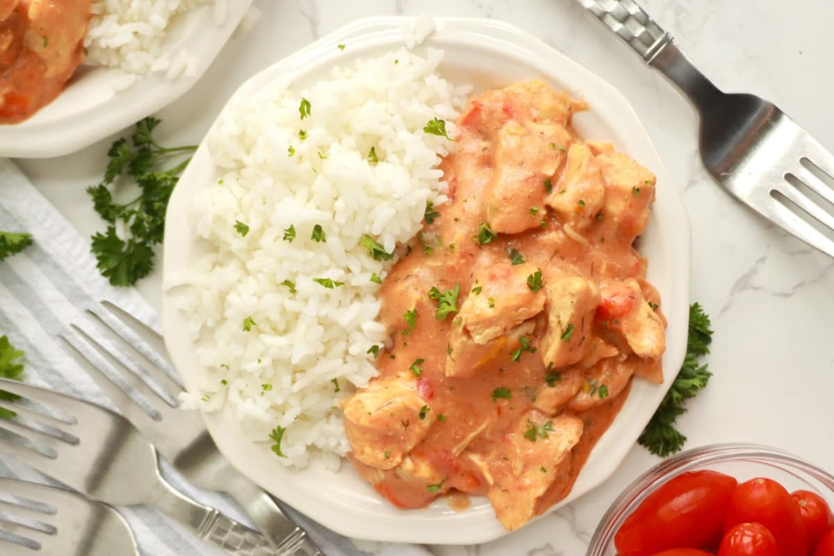 Plate of creamy tomato chicken dinners served with white rice, garnished with parsley.