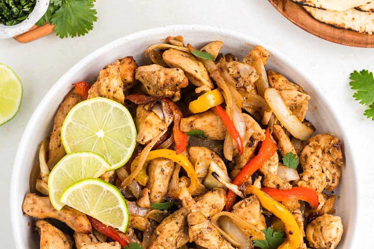 A bowl of chicken fajitas with saut&eacute;ed onions, bell peppers, and lime slices, garnished with fresh cilantro, prepared in 30 minutes or less.