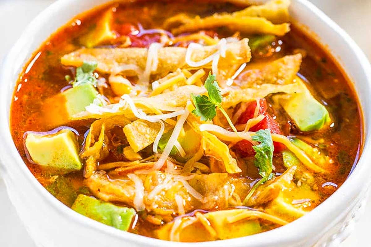 A 30-minute bowl of tortilla soup garnished with avocado slices, shredded cheese, and crisp tortilla strips.