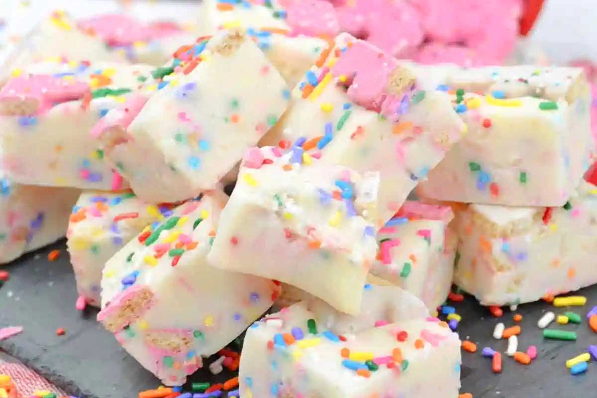 Stack of white chocolate fudge sprinkled with colorful sugar sprinkles and circus animal cookies on a slate plate.