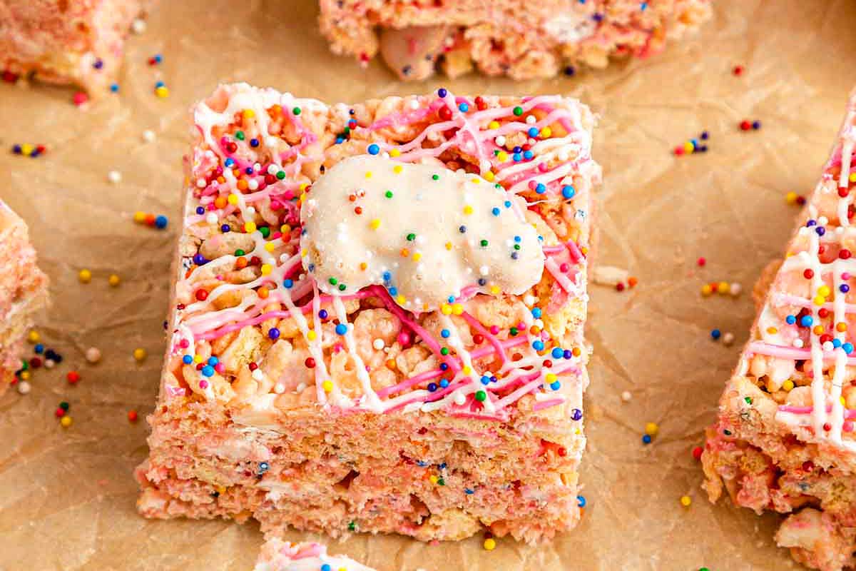 Close-up of a strawberry rice cereal treat topped with pink frosting and colorful sprinkles, inspired by recipes that use circus animal cookies, served on parchment paper.