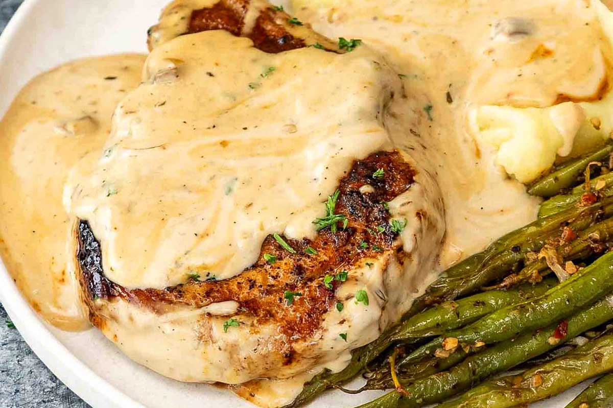 A plate of pork chop fried steak with creamy gravy, mashed potatoes, and green beans.