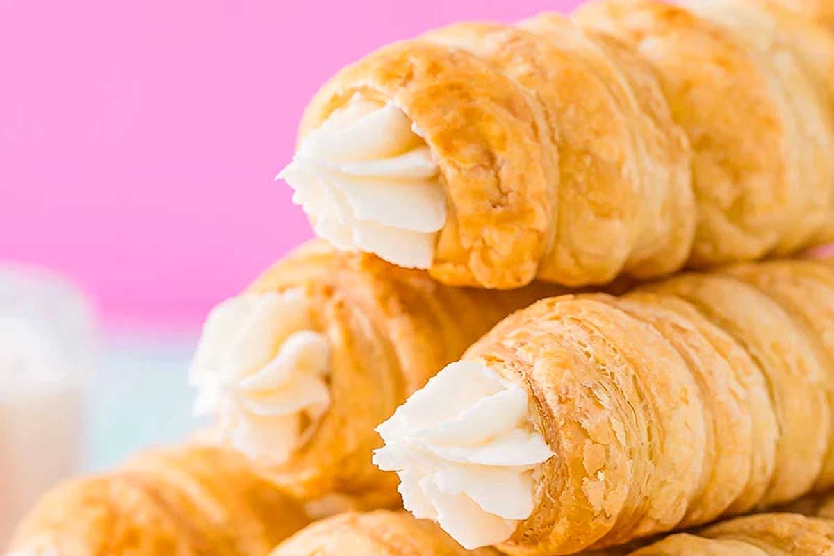 Stack of creamy, flaky croissants on a pink background.