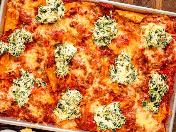 Baked lasagna in a rectangular pan topped with melted cheese, meat sauce, and dollops of spinach ricotta—an irresistible twist on classic sheet pan recipes.