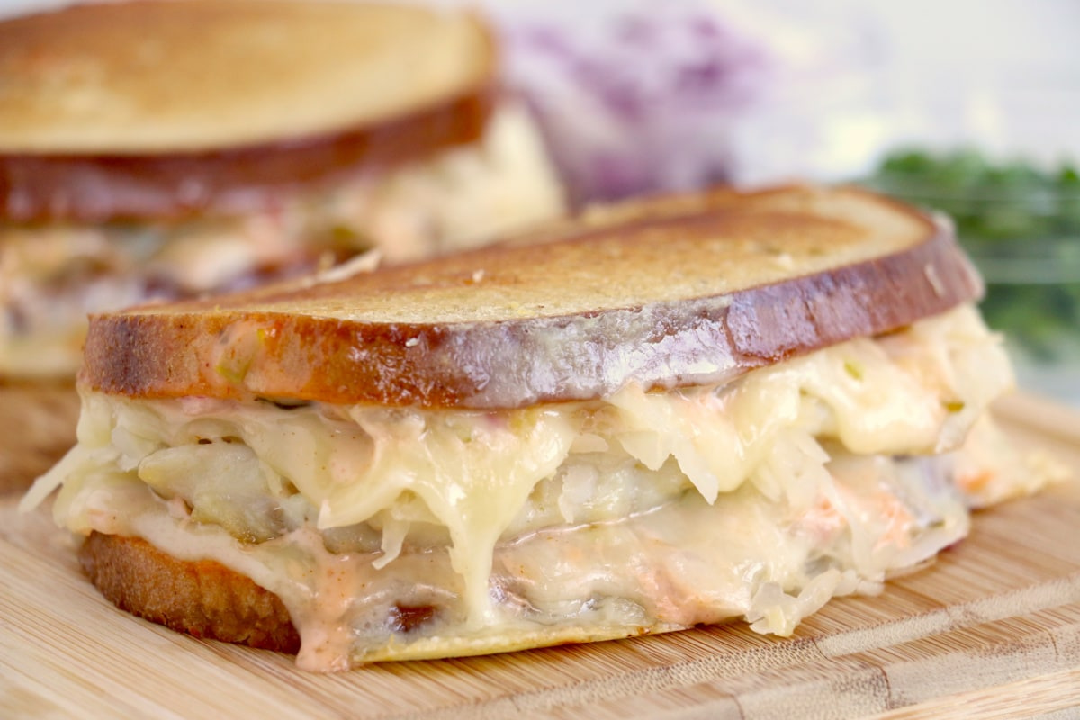 Two grilled Reuben sandwiches with melted cheese and sauerkraut on a wooden board—perfect to pair with your favorite ketchup recipes.