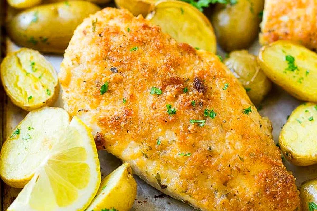 Breaded chicken breast cooked using sheet pan recipes, served with roasted potatoes and garnished with lemon slices and parsley.