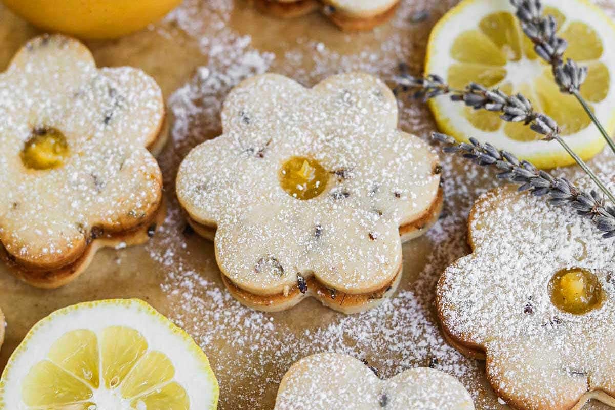 Lemon-flavored flower-shaped cookies with lemon curd centers from curated recipes, dusted with powdered sugar, adorned with lavender sprigs.