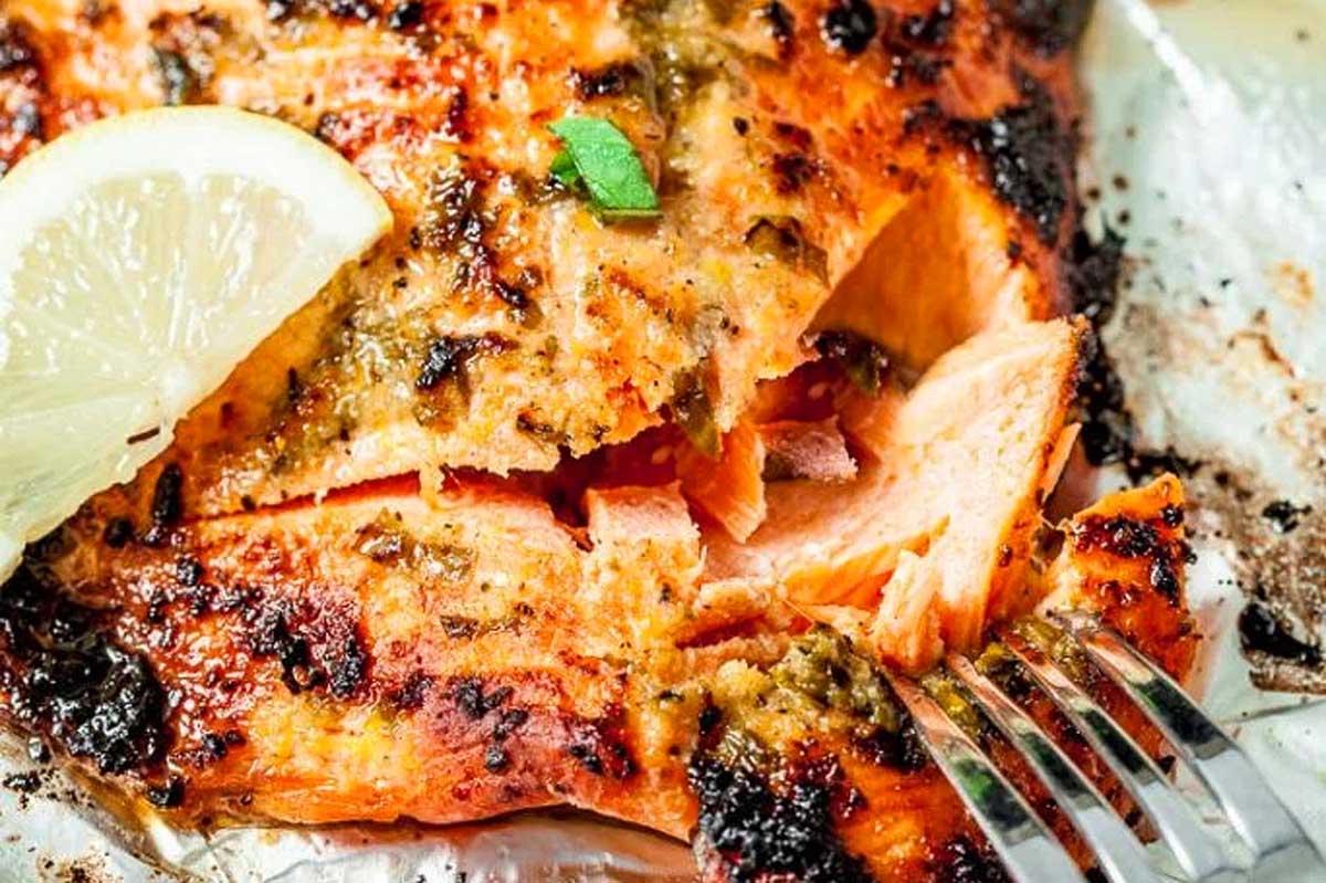 Grilled salmon fillet with crispy skin, garnished with lemon and herbs on a sheet pan.