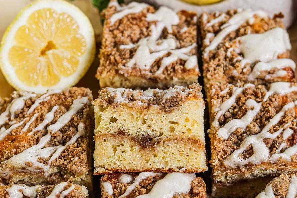 Squares of cinnamon crumb cake topped with white icing, garnished with a dollop of lemon curd on a wooden surface.