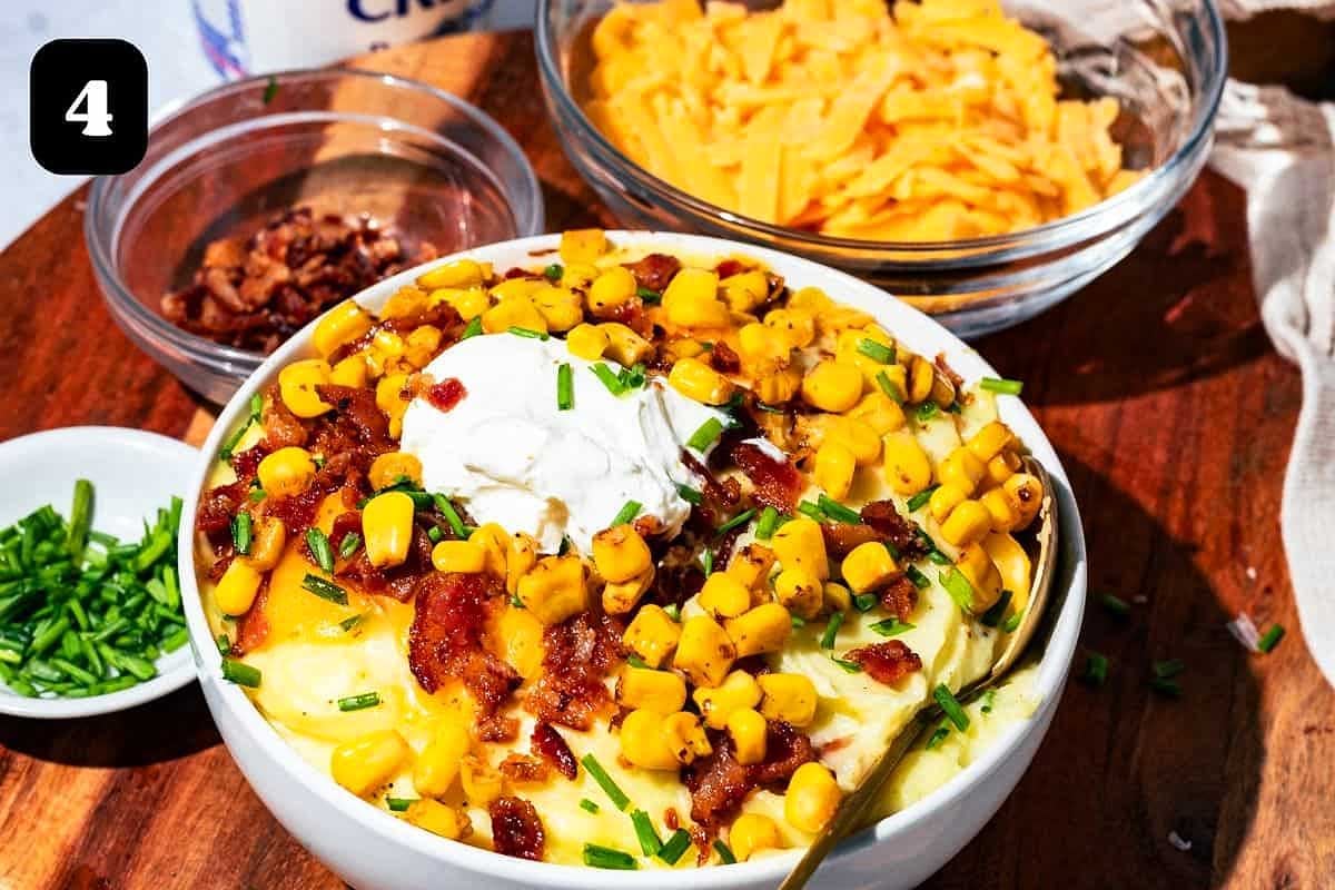A bowl of creamy mashed potatoes topped with corn, bacon, sour cream, and chives, inspired by KFC recipes, with ingredients displayed in separate bowls nearby.