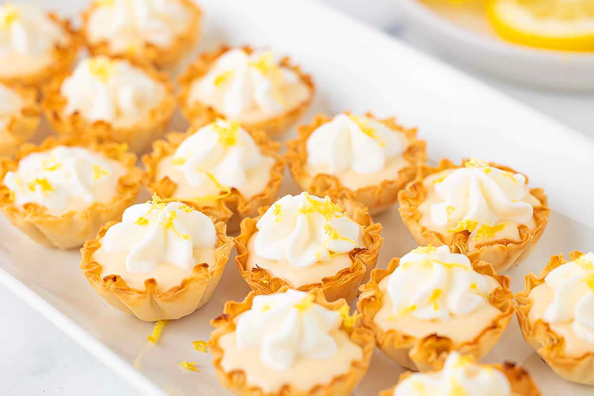 A tray of lemon curd tartlets topped with whipped cream and lemon zest.