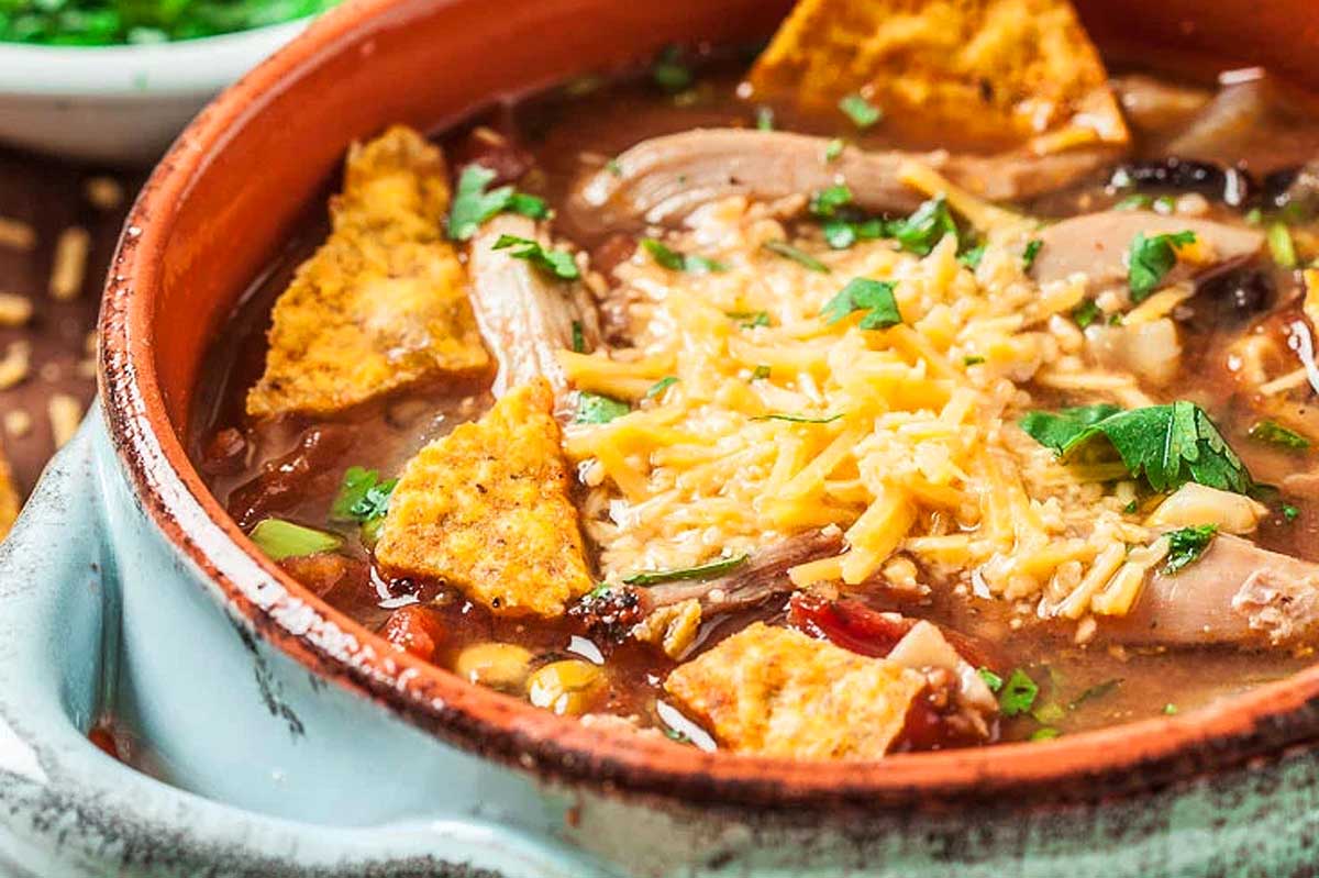 A bowl of tortilla soup garnished with shredded cheese, diced tomatoes, and parsley, prepared in 30 minutes or less, served with crispy tortilla strips on top.