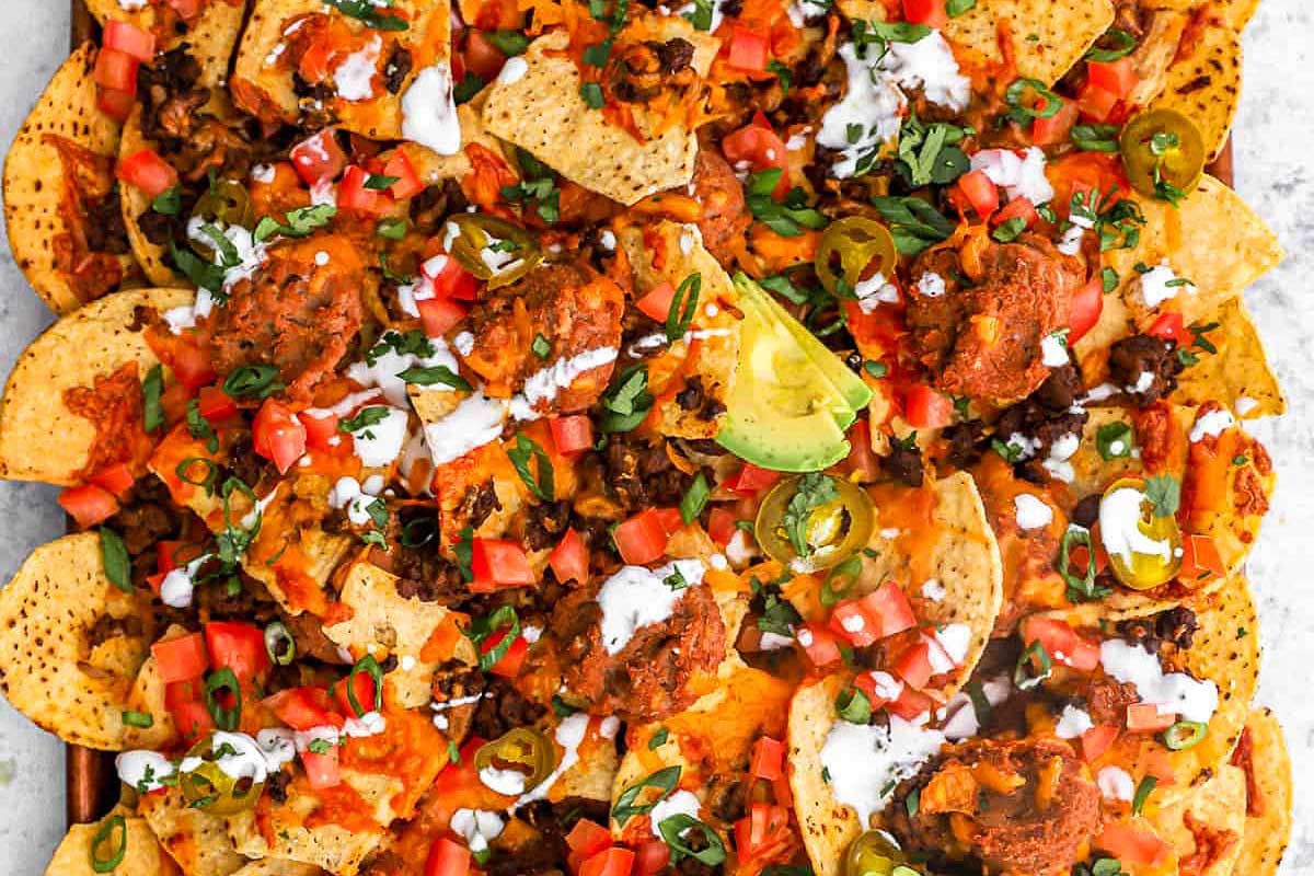 A plate of nachos topped with shredded meat, diced tomatoes, jalapeños, sour cream, and garnished with fresh cilantro and lime wedges, inspired by Taco Bell copycat recipes.