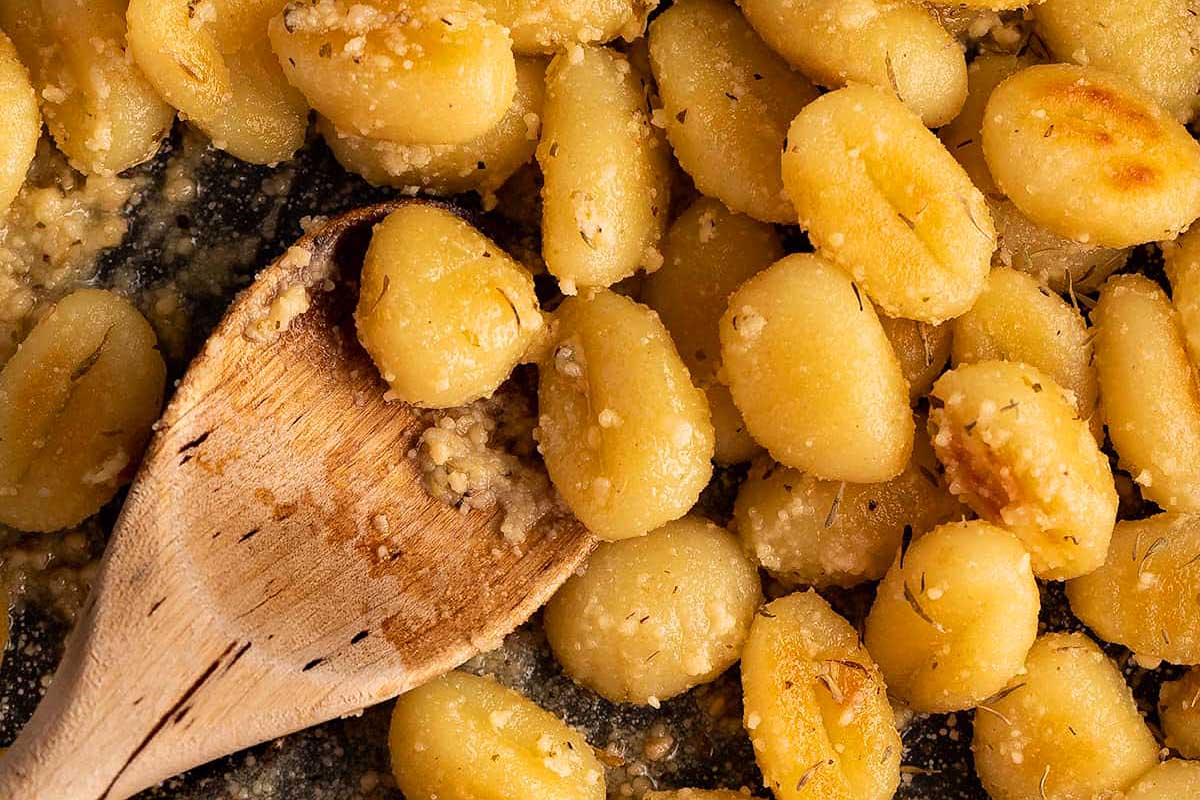 Close-up of saut&eacute;ed gnocchi with garlic and herbs on a wooden spoon, garnished with parmesan cheese, all made in 30 minutes or less, over a dark pan
