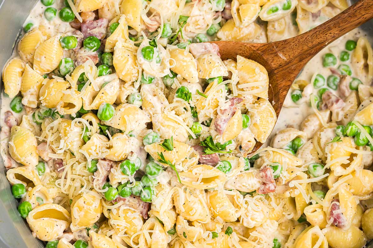 Creamy pasta shells with peas, crispy pancetta, and grated cheese, stirred with a wooden spoon for a perfect pancetta pea pasta.
