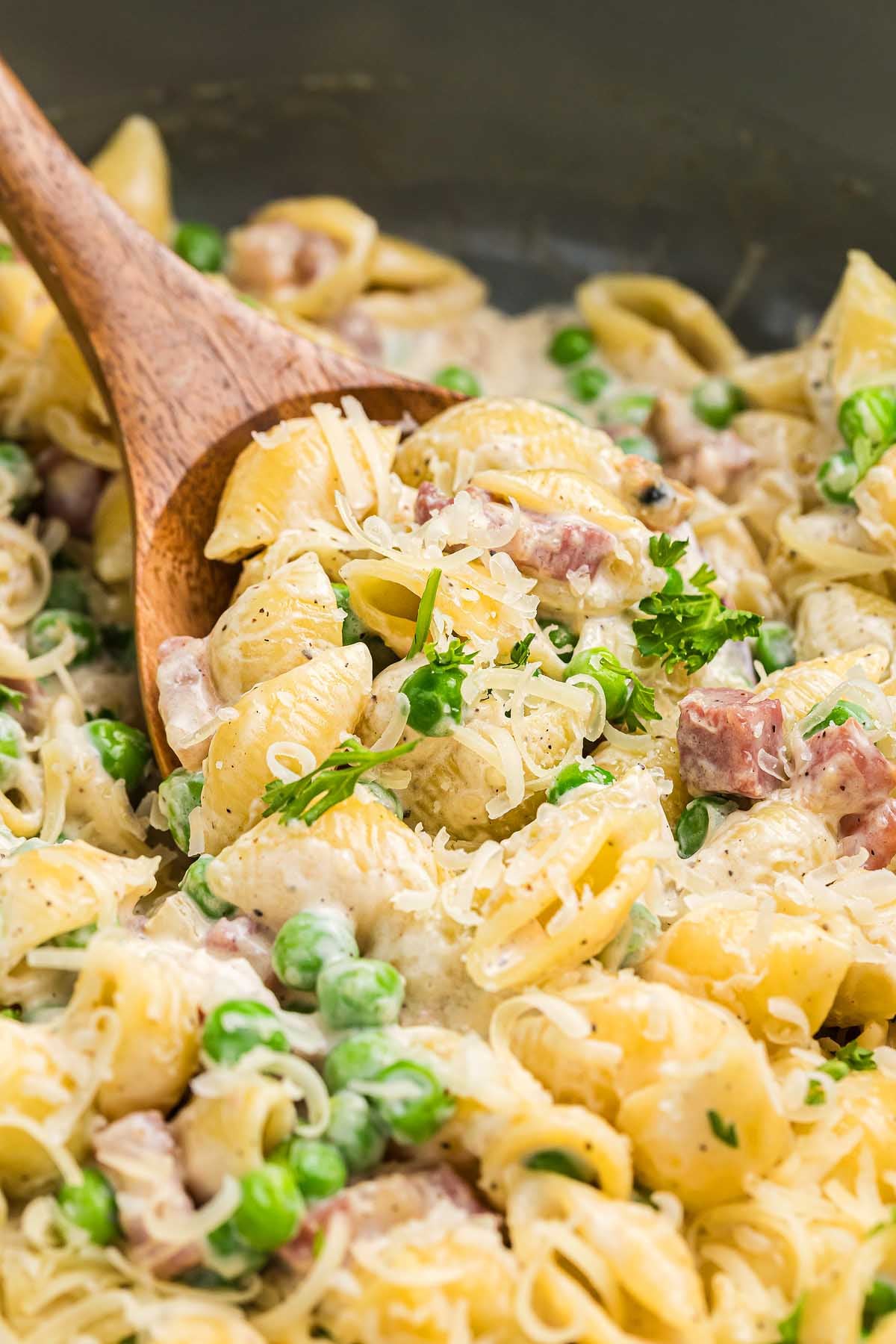 Creamy pancetta pea pasta shells with ham and parsley, being stirred gently with a wooden spoon.