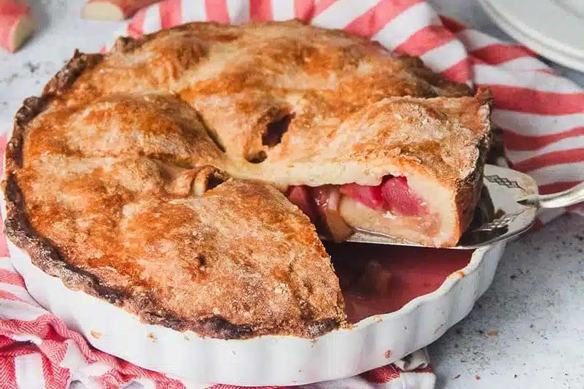 Freshly baked rhubarb pie with a flaky crust, served in a white dish, with one slice partially removed.
