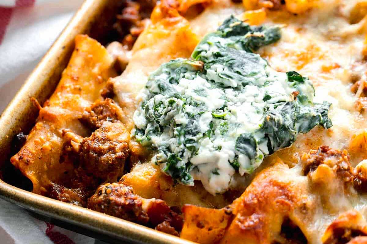 Baked pasta dish with melted cheese and spinach topping in a sheet pan.