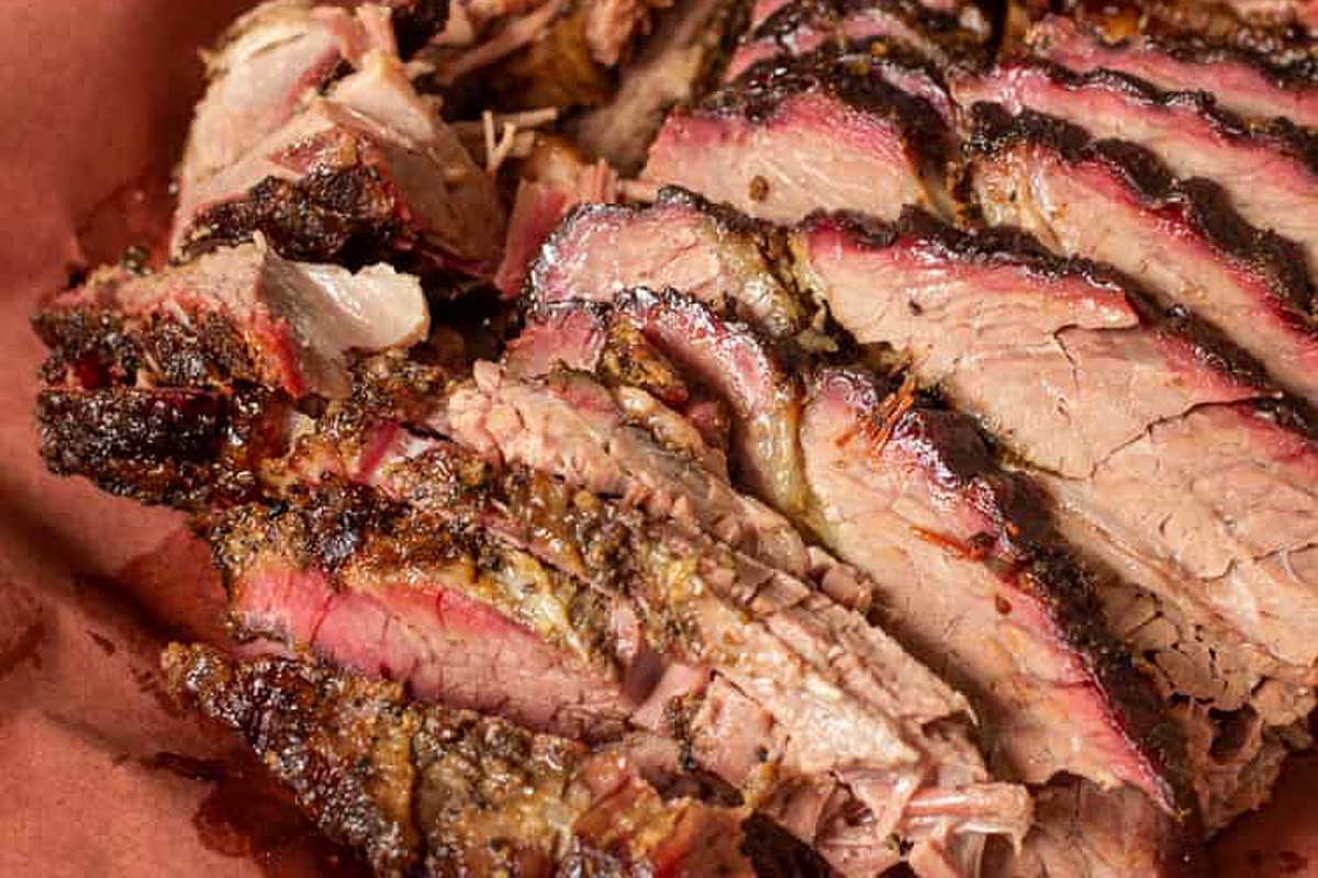 Sliced smoked beef brisket from smoker recipes, with a charred crust and visible pink smoke ring, served on brown butcher paper.