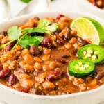 A bowl of slow cooker cowboy beans topped with cilantro, sliced jalapeños, and a lime wedge.