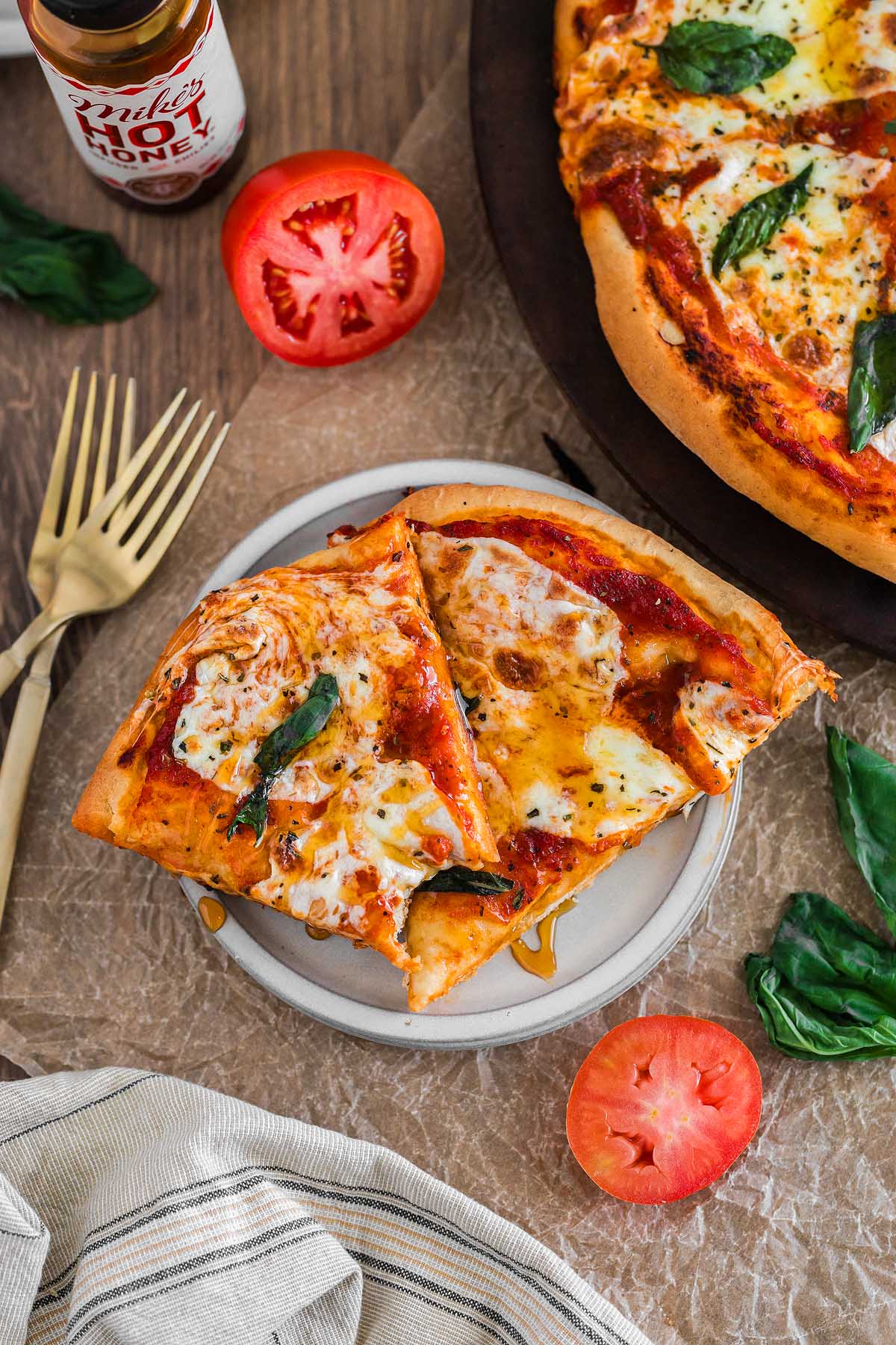 Two slices of margherita pizza with basil and cheese rest on a plate, surrounded by fresh tomato and basil leaves, capturing the classic flavors of traditional margherita pizza.