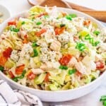A bowl of chopped chicken blue cheese salad with lettuce, diced tomatoes, crumbled blue cheese, and green onions on a table with wooden utensils and a small bowl of blue cheese in the background.