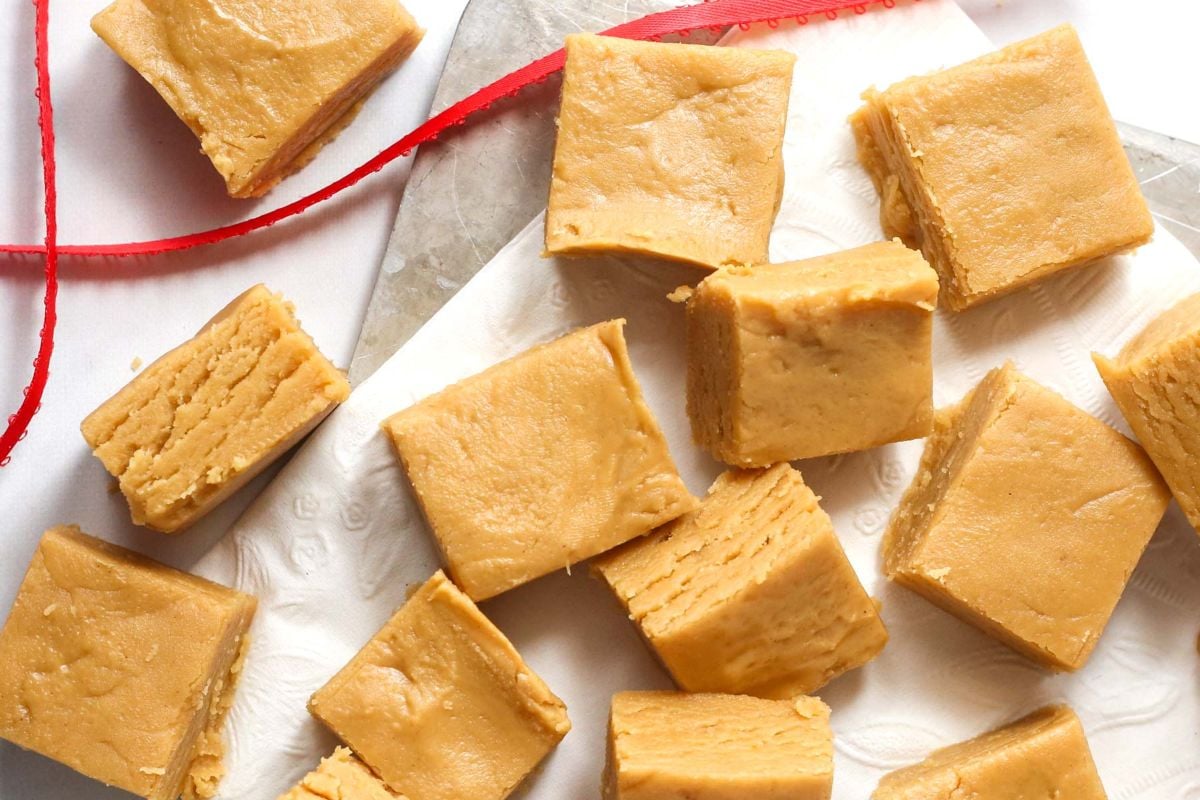 Several pieces of creamy fudge are arranged on a white paper, with a red ribbon partially visible at the top of the image — perfect shortcut desserts for any occasion.