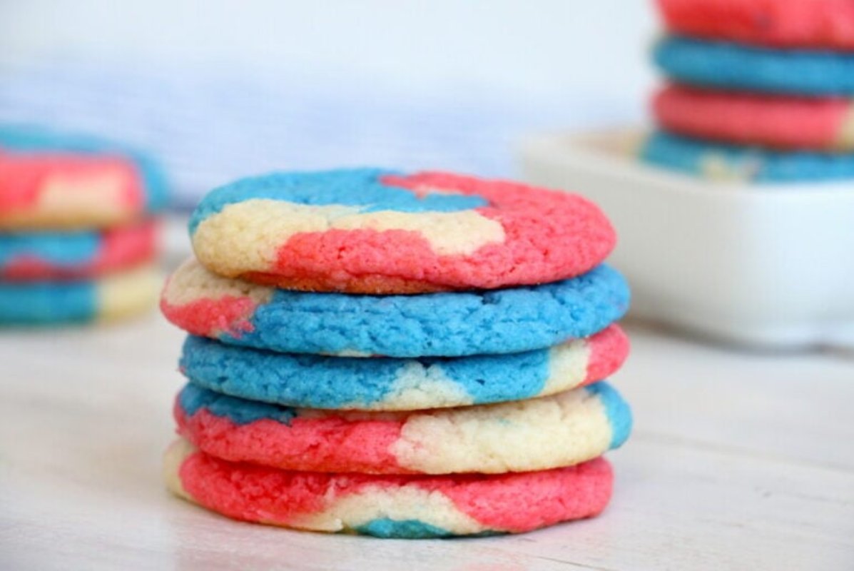 A stack of six round cookies with a marbled pattern in red, white, and blue sits on a light-colored surface, showcasing delicious Patriotic Desserts, with more cookies in the background.