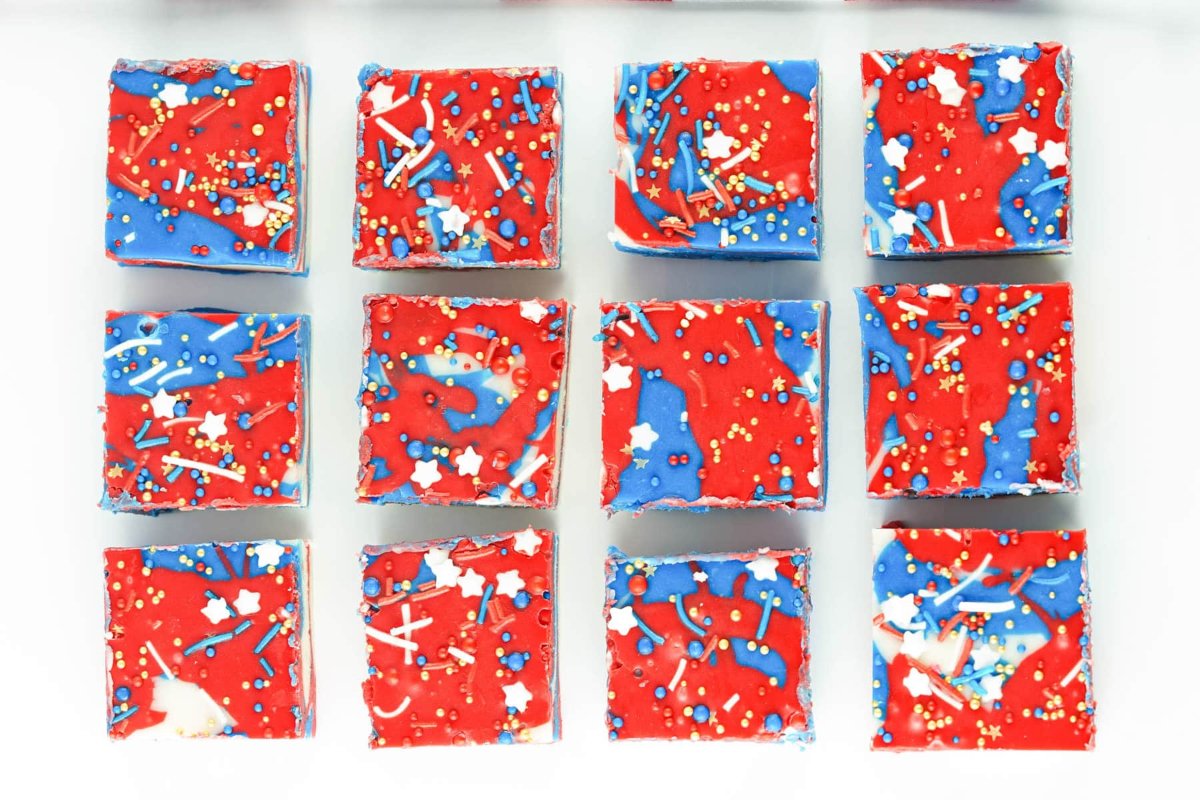 Twelve square pieces of red, white, and blue sprinkle-covered fudge arranged in a 3x4 grid on a white background make for perfect patriotic desserts.