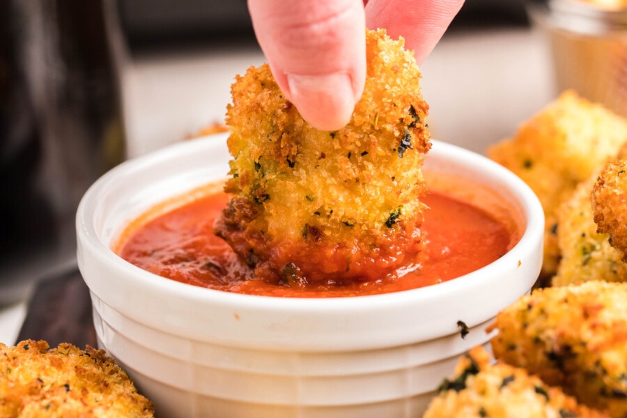 Hand dipping a breaded mozzarella stick into a bowl of marinara sauce, perfect as a cheesy appetizer to pair with your favorite chicken recipes.