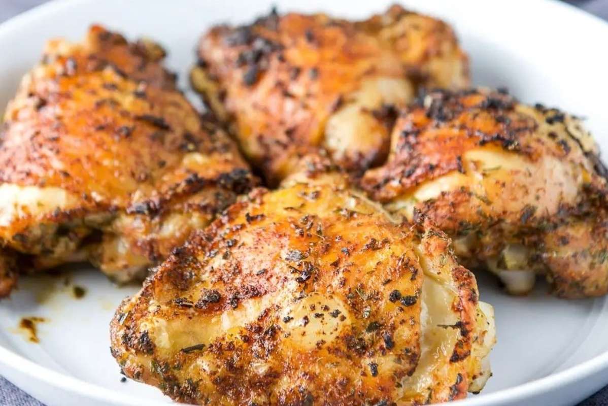 A white plate with four pieces of seasoned and cooked chicken thigh recipes, featuring crispy golden-brown skin.
