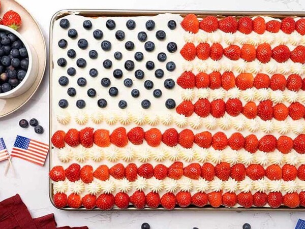 Sheet cake decorated in red, white and blue as an American flag, featuring strawberries, blueberries, and white icing stars.