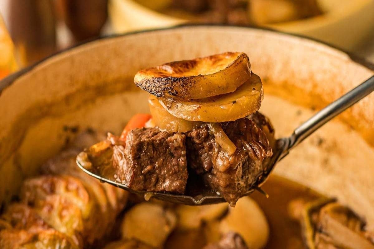 A spoonful of beef, potatoes and veggies over a baking dish of beef casserole.