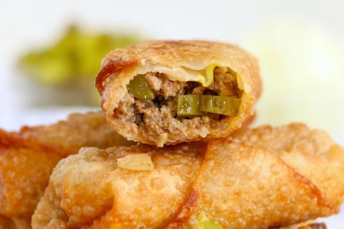 A close-up of a fried egg roll cut open, showing a filling of ground beef and pickles—perfect for those seeking Big Mac inspired recipes.