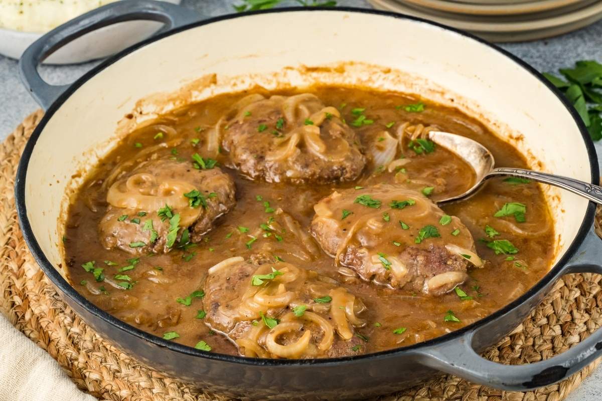 Hamburger steaks in gravy in a skillet with fresh herb garnish on top.