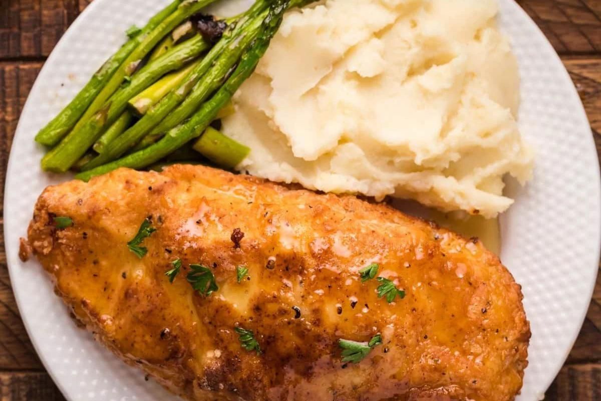 Enjoy one of our favorite chicken recipes: tender chicken breast with mashed potatoes and asparagus, all beautifully presented on a white plate and garnished with parsley.