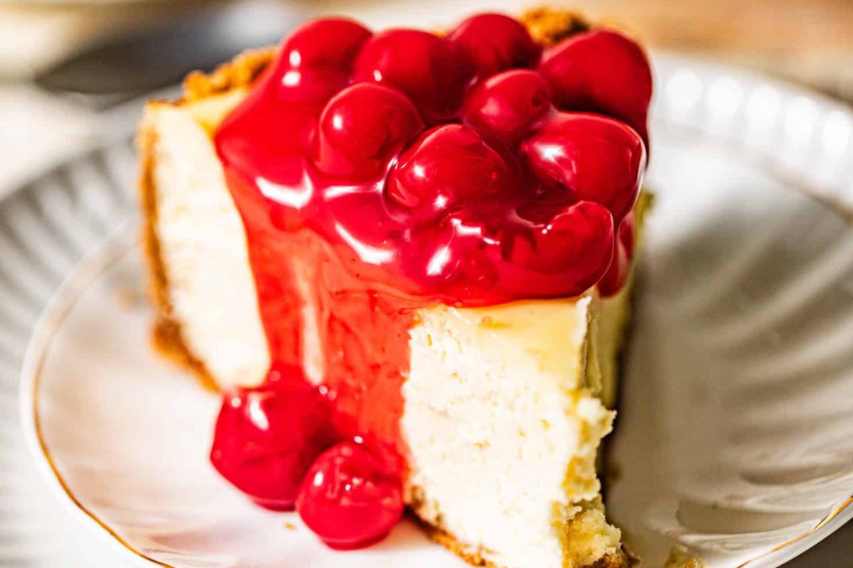 A slice of cheesecake topped with a layer of bright red cherry sauce on a white plate, perfect for exploring new cherry recipes.