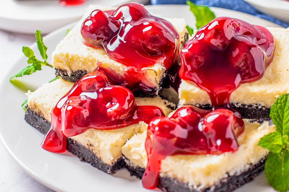 A plate of cheesecake bars topped with a generous amount of cherry sauce, garnished with mint leaves—one of the finest cherry recipes you can try.