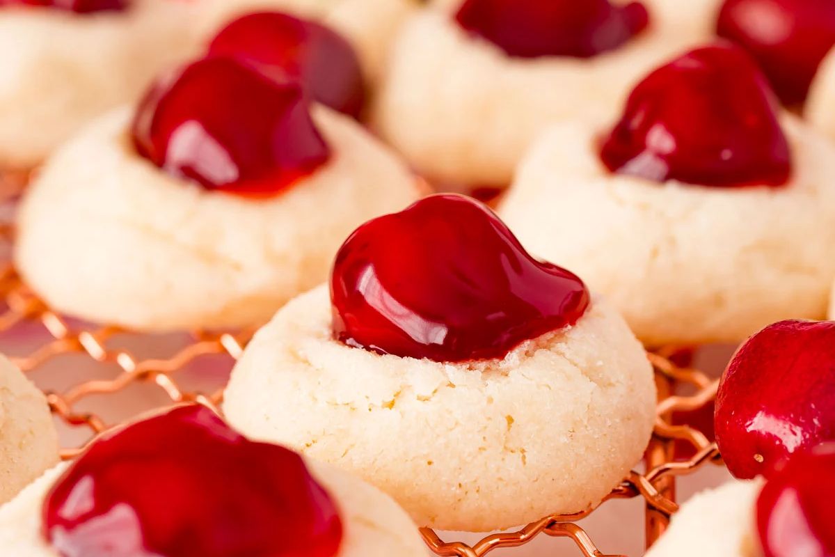 Close-up of thumbprint cookies with dollops of red cherry filling in the center, cooling on a wire rack—perfect for all your favorite cherry recipes.