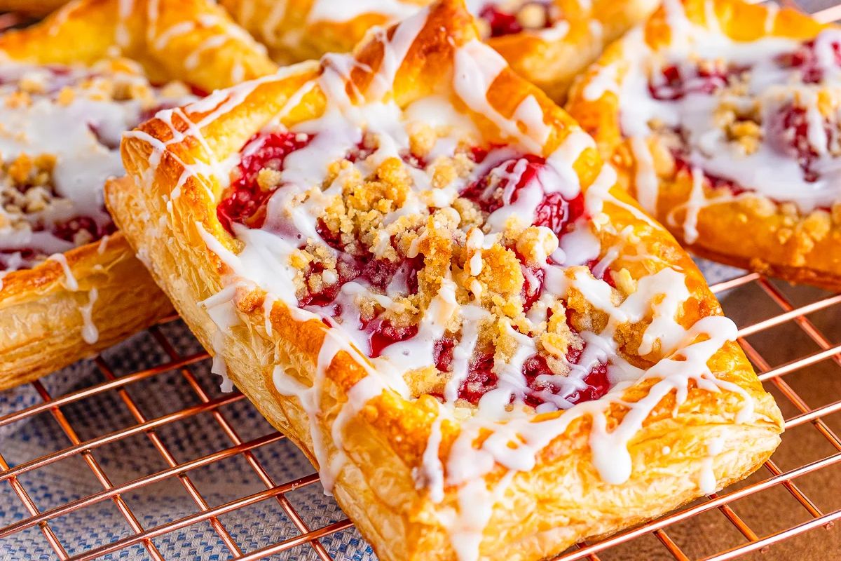 Close-up of cherry danishes with a crumble topping and white icing, cooling on a wire rack. Perfect for fans of cherry recipes looking to indulge in a delicious treat!
